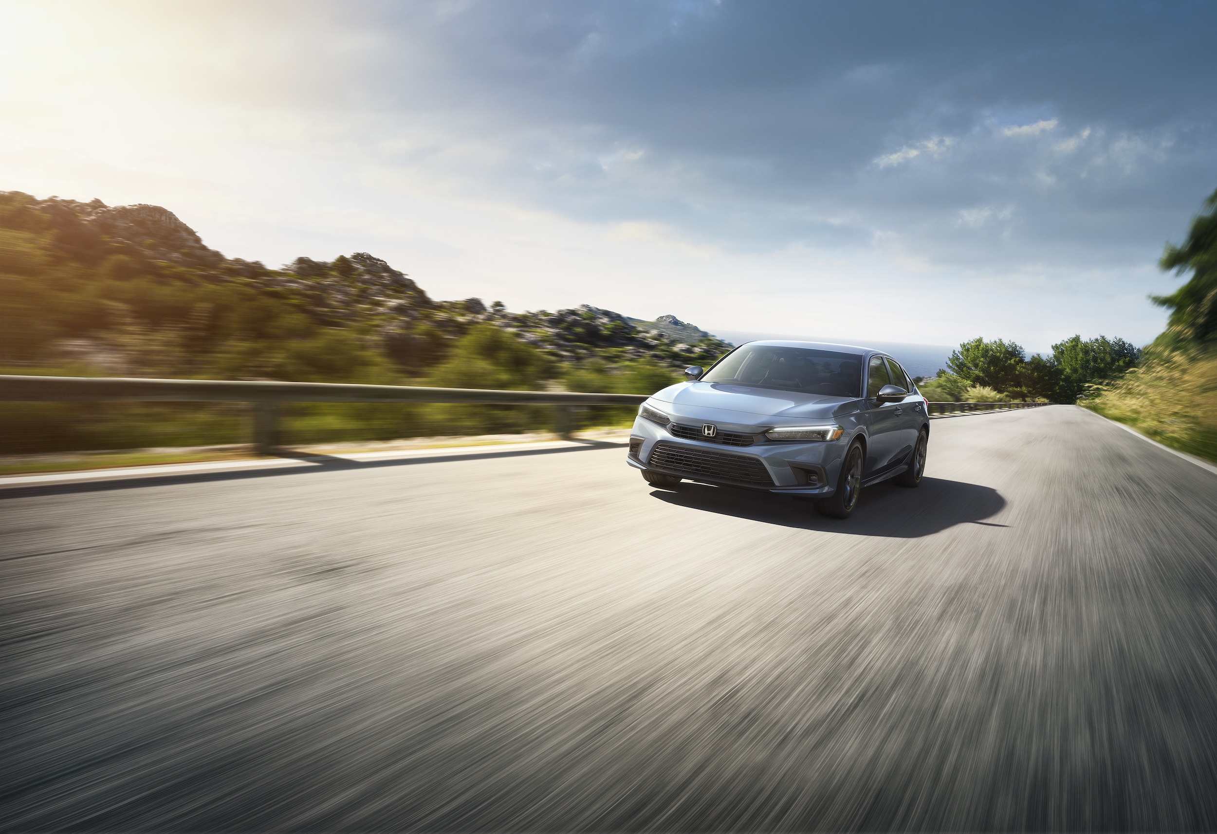 silver Honda Civic Sport driving fast on a road with guard rail and shrub lined hills