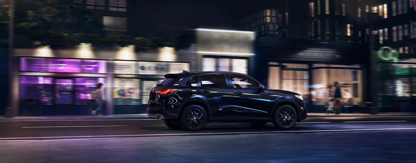 A black 2025 Honda HR-V Sport is driving on a city street at night.