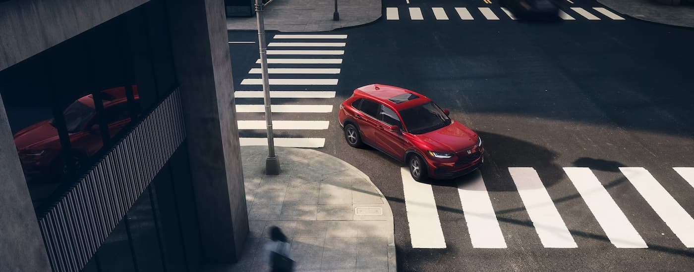 A red 2024 Honda HR-V EX-L is driving on a city street.