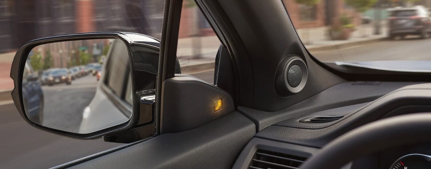 A close-up shows the illuminated blind spot monitoring icon in a black 2021 Honda Passport.