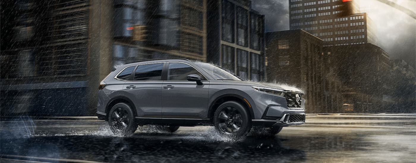 A grey 2024 Honda CR-V Hybrid Sport Touring is driving through a city on a rainy day.