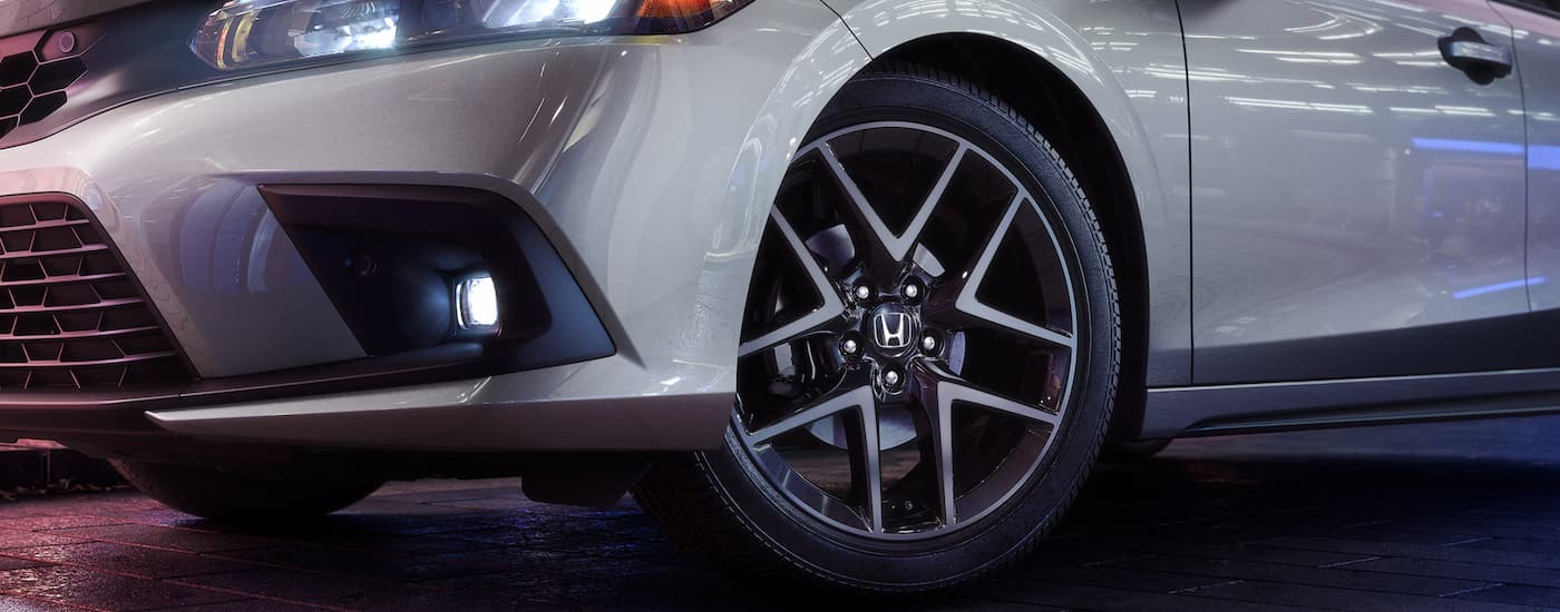 A close up of the front and tire on a silver 2024 Honda Civic Hatchback Sport Touring at a Honda dealer near Grosse Ile Township.