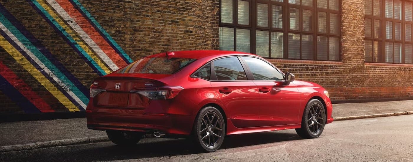 Red 2024 Honda Civic Sport driving by a brick wall.