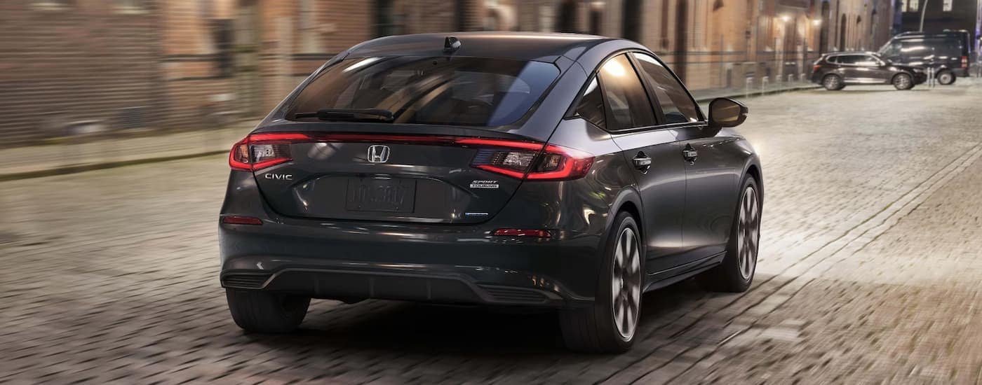 Black 2025 Honda Civic Sport Touring Hybrid driving down a road.