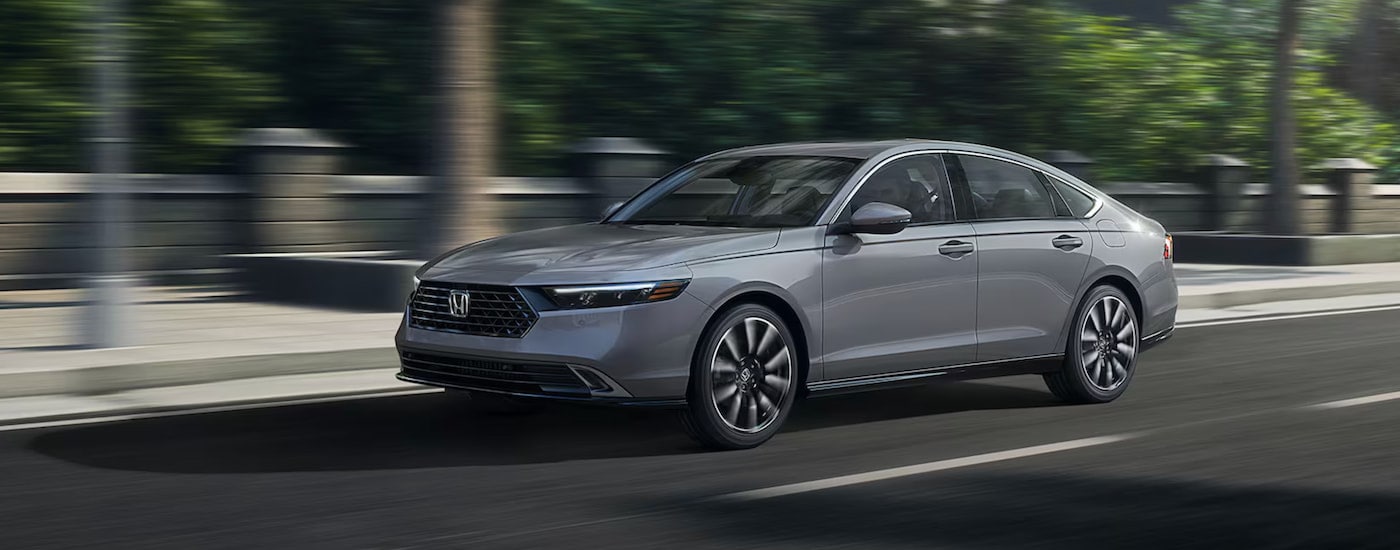 A silver 2025 Honda Accord Hybrid Touring driving downtown.