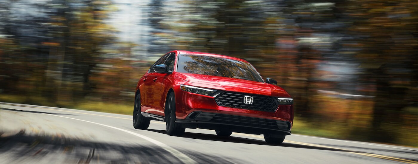 Head-on view of a red 2024 Honda Accord Hybrid Sport-L driving an on open road.
