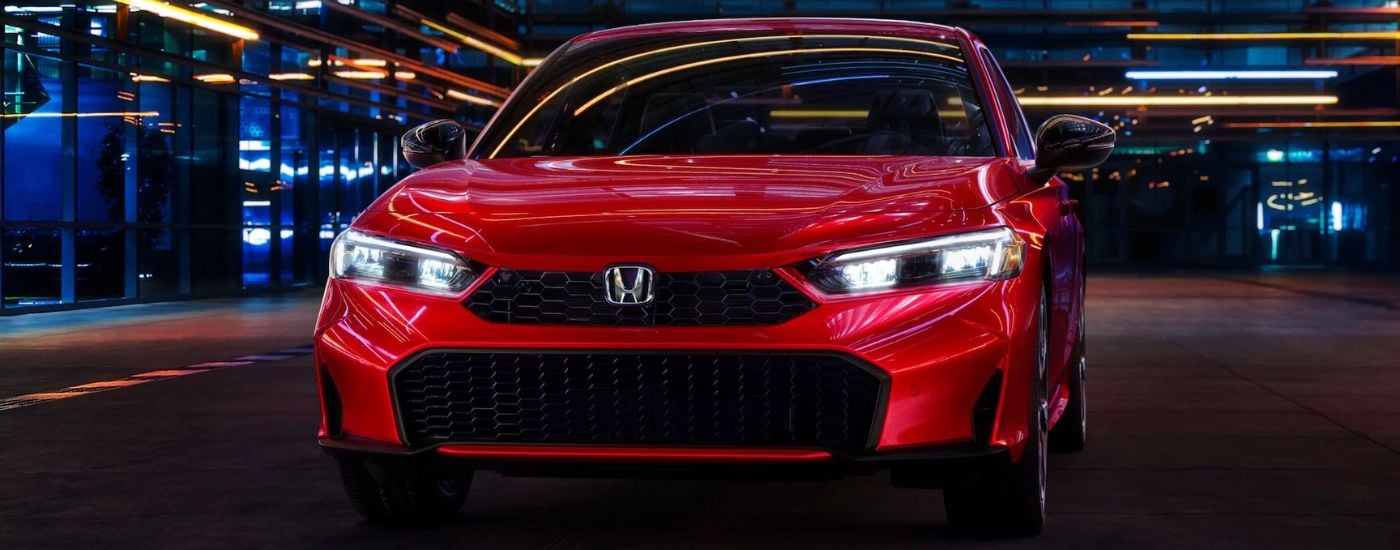A red 2025 Honda Civic Hybrid Sport Touring under neon lights at night.
