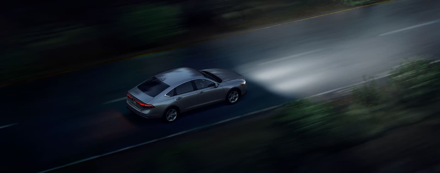 Grey 2025 Honda Acorrd LX Hybrid driving on a road at night