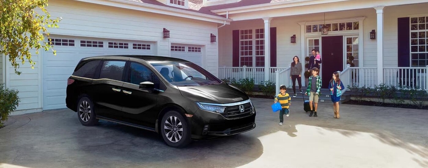 A black 2023 Honda Odyssey is shown parked in front of a garage.