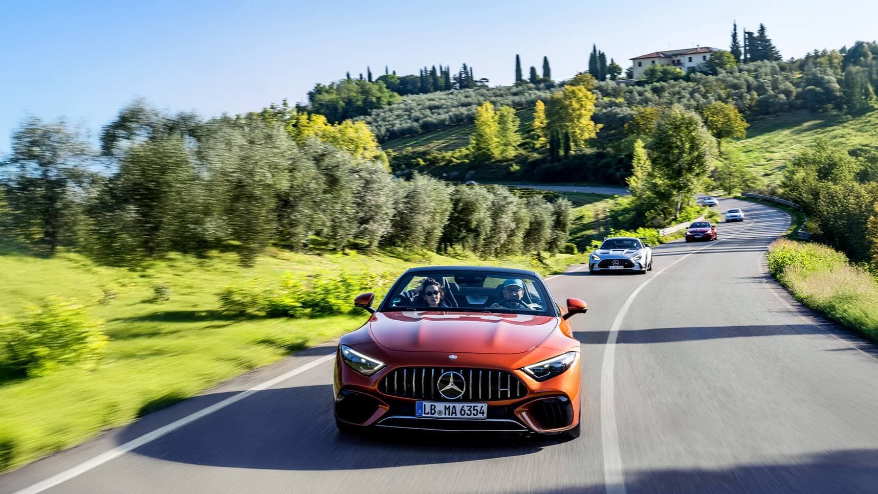 An orange Mercedes-AMG® roaster leading a line of Mercedes-AMG® vehicles down a countryside road
