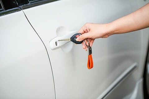 person holding their car key up to their car door