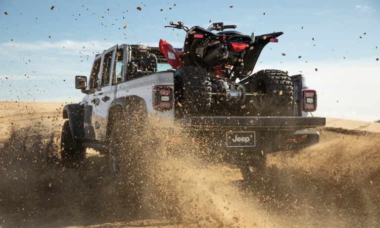 2025 Jeep Gladiator kicking up mud with ATV in back