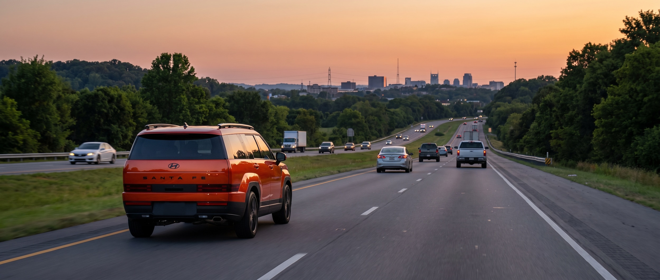A 2026 Hyundai Santa Fe Hybrid in a bold exterior color driving along a Tennessee interstate at dusk, light traffic visible ahead, suburban Nashville skyline in the background, warm summer light