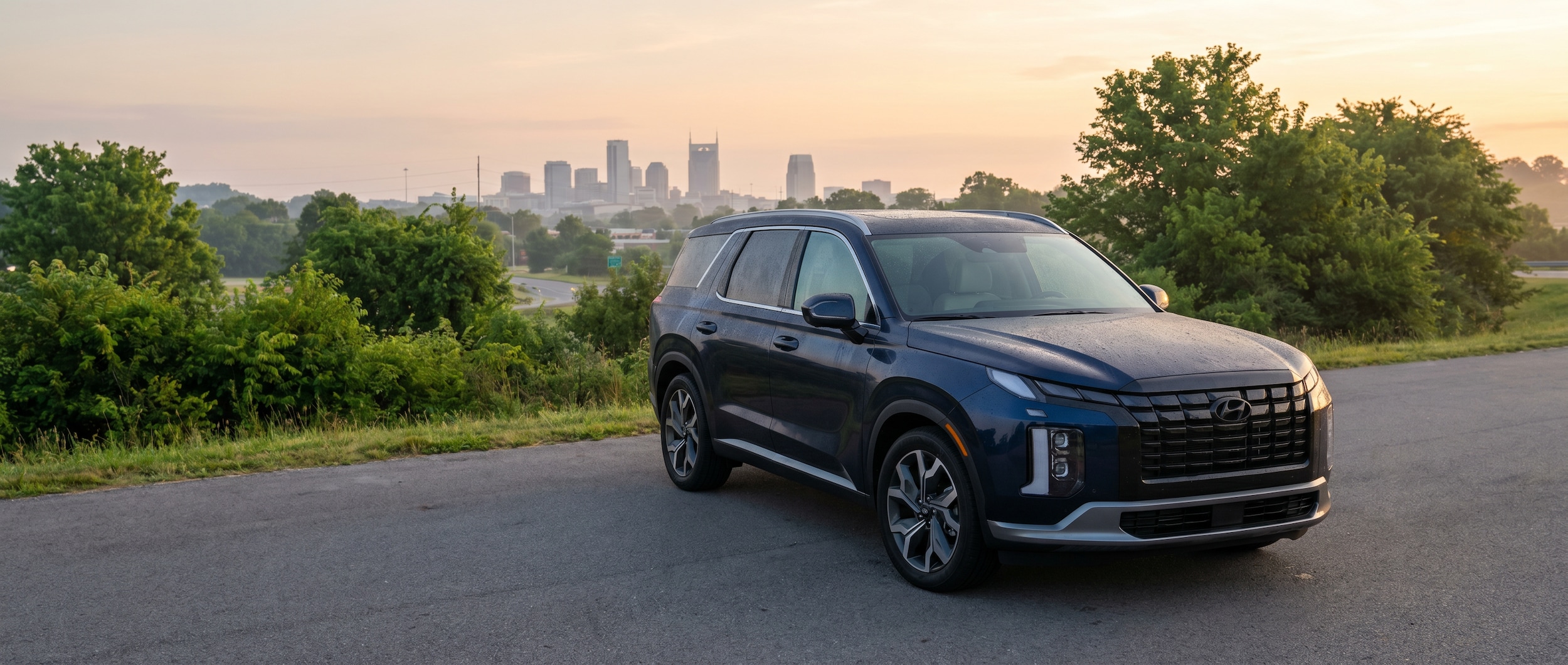 A 2026 Hyundai Palisade in dark blue or silver parked along a Middle Tennessee highway on-ramp at dawn, with the Nashville skyline faintly visible in the background and green summer foliage lining the road -- conveying a confident, capable family SUV ready for the daily commute
