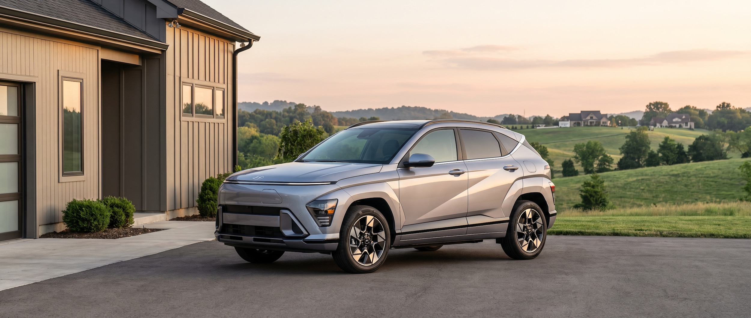 A 2026 Hyundai Kona Electric in a modern suburban driveway at dawn, plugged into a home Level 2 charger, with a Tennessee landscape of rolling green hills visible in the background suggesting a South Nashville suburb