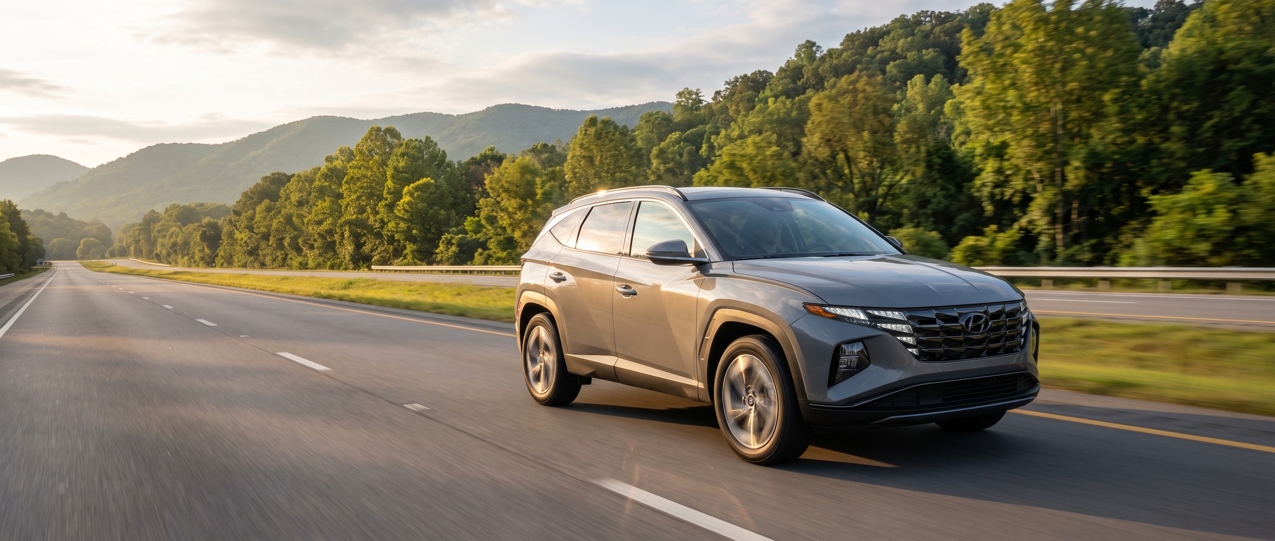 A 2026 Hyundai Tucson in Ecotronic Gray driving south on a Tennessee interstate corridor in morning light, dashboard visible through the windshield, suburban exits and green highway signage in the background, conveying a confident weekday commute.
