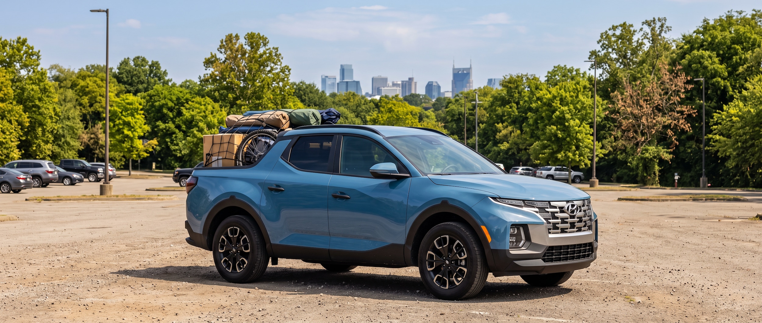 2026 Hyundai Santa Cruz SEL Activity in Calypso Blue parked in a large Nashville-area outdoor lot surrounded by trees in late-summer heat, with a full truck bed and suburban Nashville skyline visible in the distance.