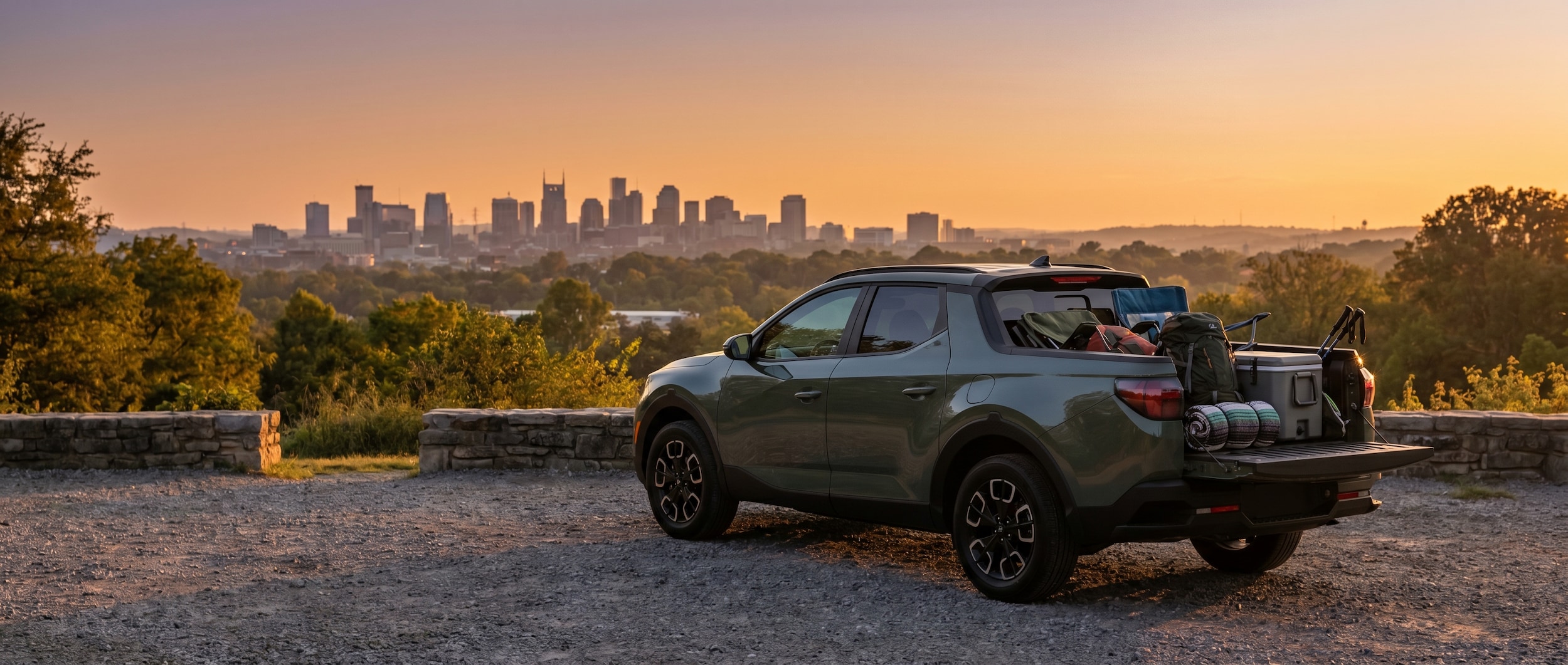 A Hyundai Santa Cruz parked at Percy Warner Park overlook during golden hour, showcasing Nashville skyline in the background with the truck bed loaded with outdoor gear