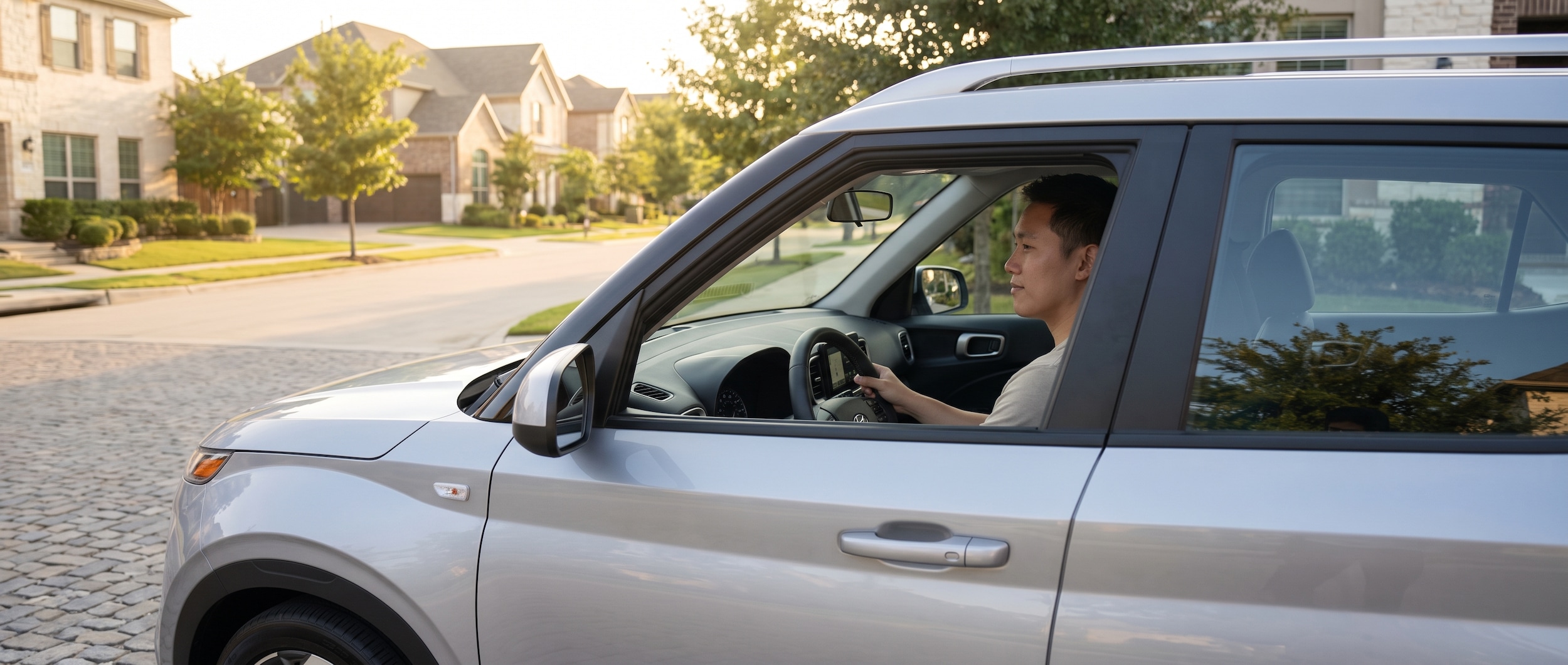 A Hyundai Venue in a modern urban setting with suburban streets in the background, soft afternoon light, driver-focused interior visible through window, conveying confidence and everyday practicality.