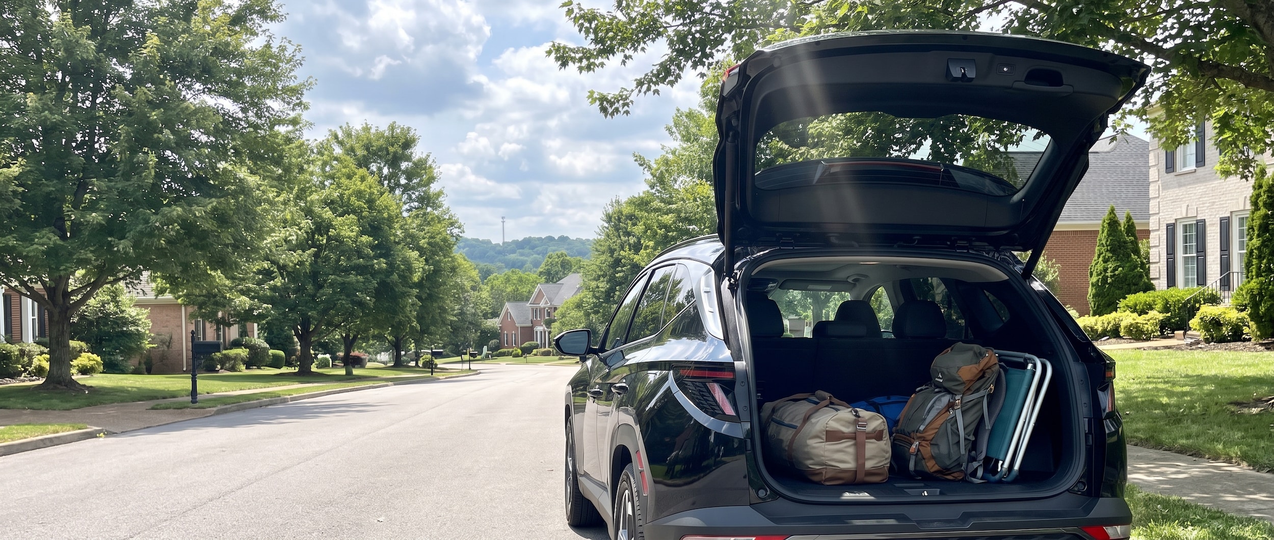 A 2026 Hyundai Tucson in Midnight Black Metallic parked in a suburban Nashville setting on a bright August morning, rear hatch open revealing a loaded cargo area with a backpack and sports bag, Tennessee summer sky in the background.