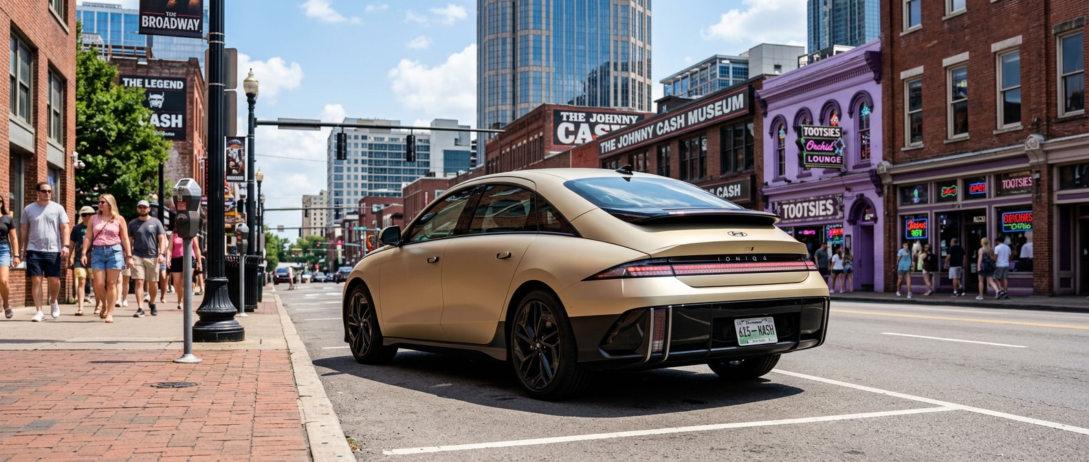 2025 Hyundai IONIQ 6 in Gravity Gold Matte parked on a sunlit Nashville downtown street with the distinctive LED pixel light signature visible, low-profile sedan silhouette against urban architecture, August midday light
