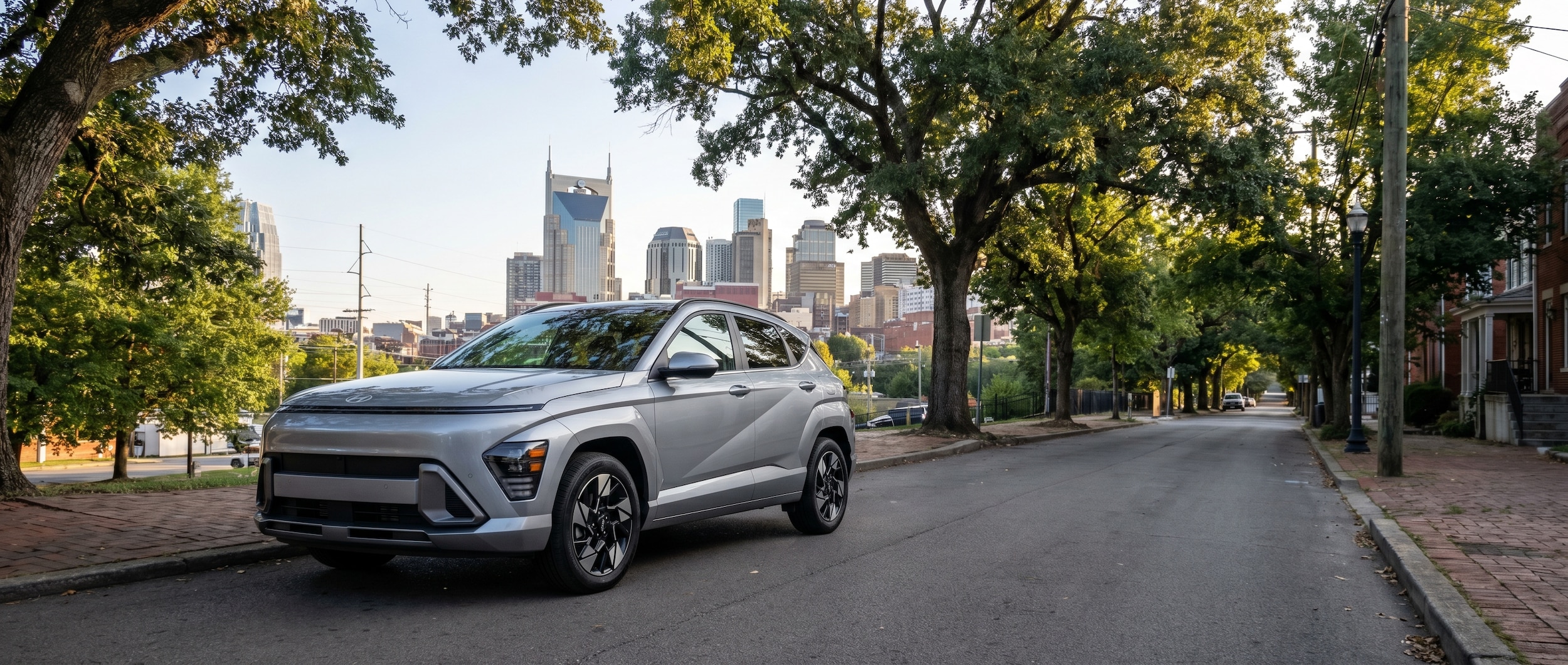 A silver Hyundai Kona parked along a tree-lined urban road in Nashville, Tennessee, with the city skyline softly visible in the background on a clear afternoon