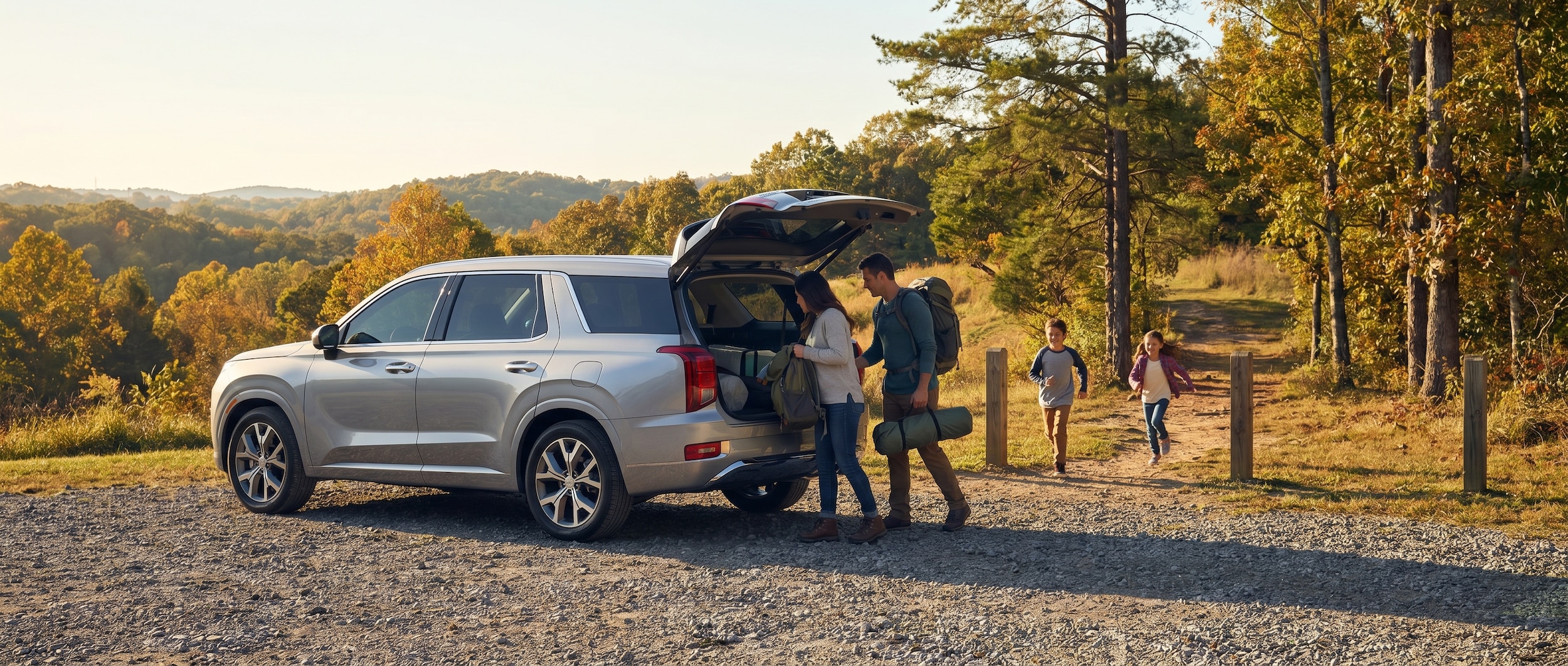 A silver Hyundai Palisade parked in front of a scenic Tennessee park entrance with a family of four unloading gear and children running toward a trail on a sunny day.