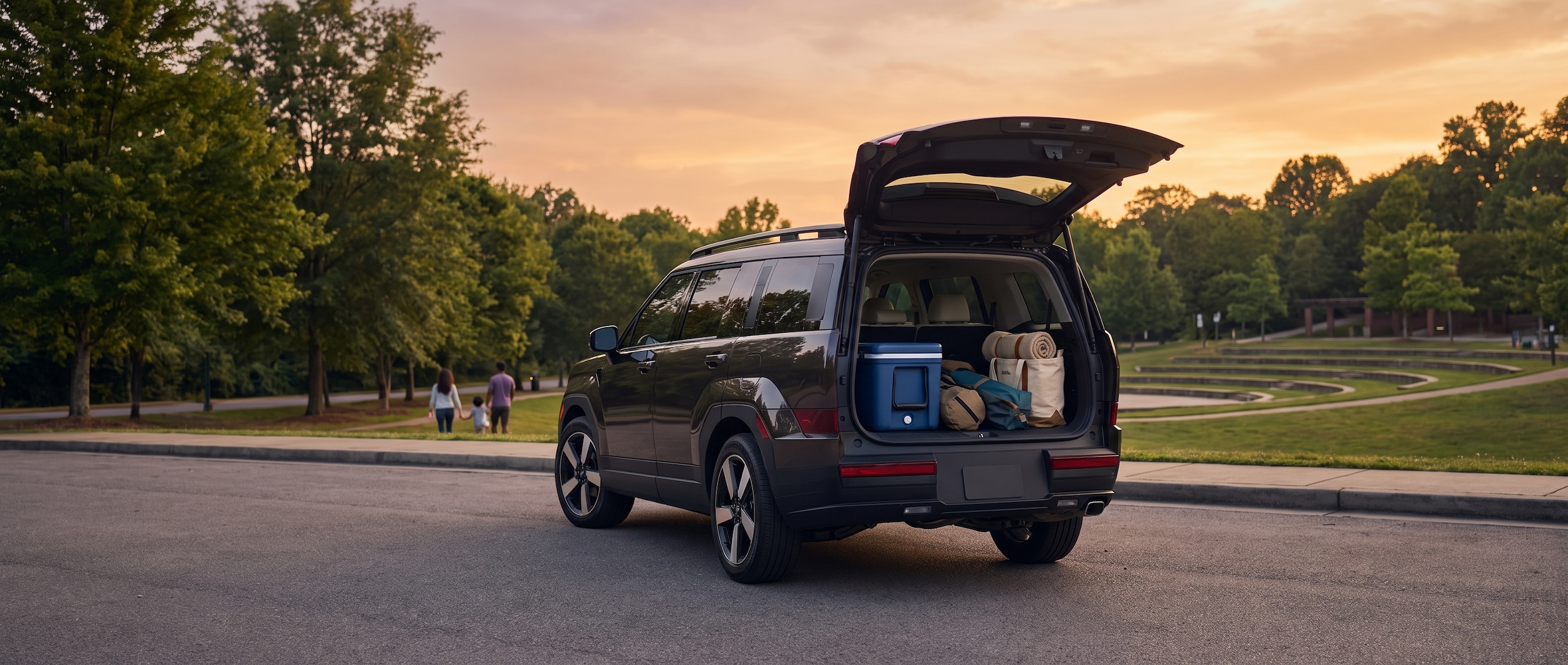 A 2026 Hyundai Santa Fe parked in a suburban lot at golden hour, rear liftgate open revealing a neatly loaded cooler, folding chairs, and a blanket bag -- a family-ready setup before a summer outdoor concert. Warm Tennessee sky in the background.