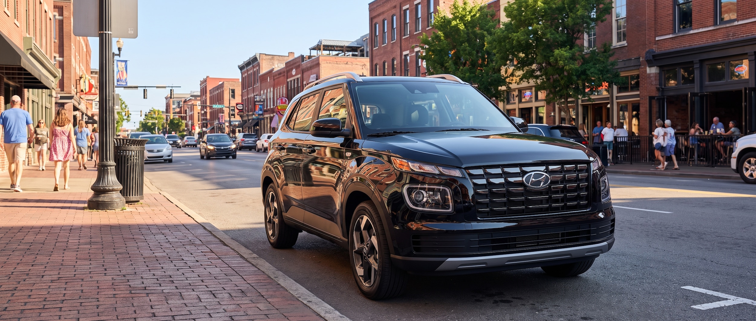 A 2026 Hyundai Venue in Onyx Black parked on a Nashville urban street in summer light, with a busy commercial corridor visible in the background, shot from the front three-quarter angle emphasizing the compact proportions and modern front fascia