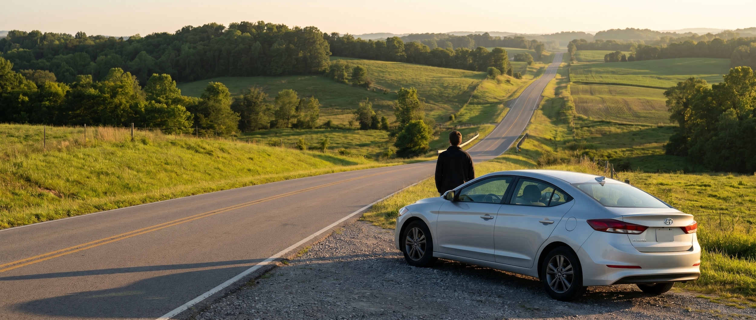 A silver Hyundai Elantra parked along a scenic Tennessee highway at golden hour, with rolling green hills and open road stretching into the distance, conveying freedom and adventure