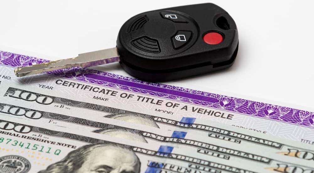 A key fob is on a vehicle's title and money.