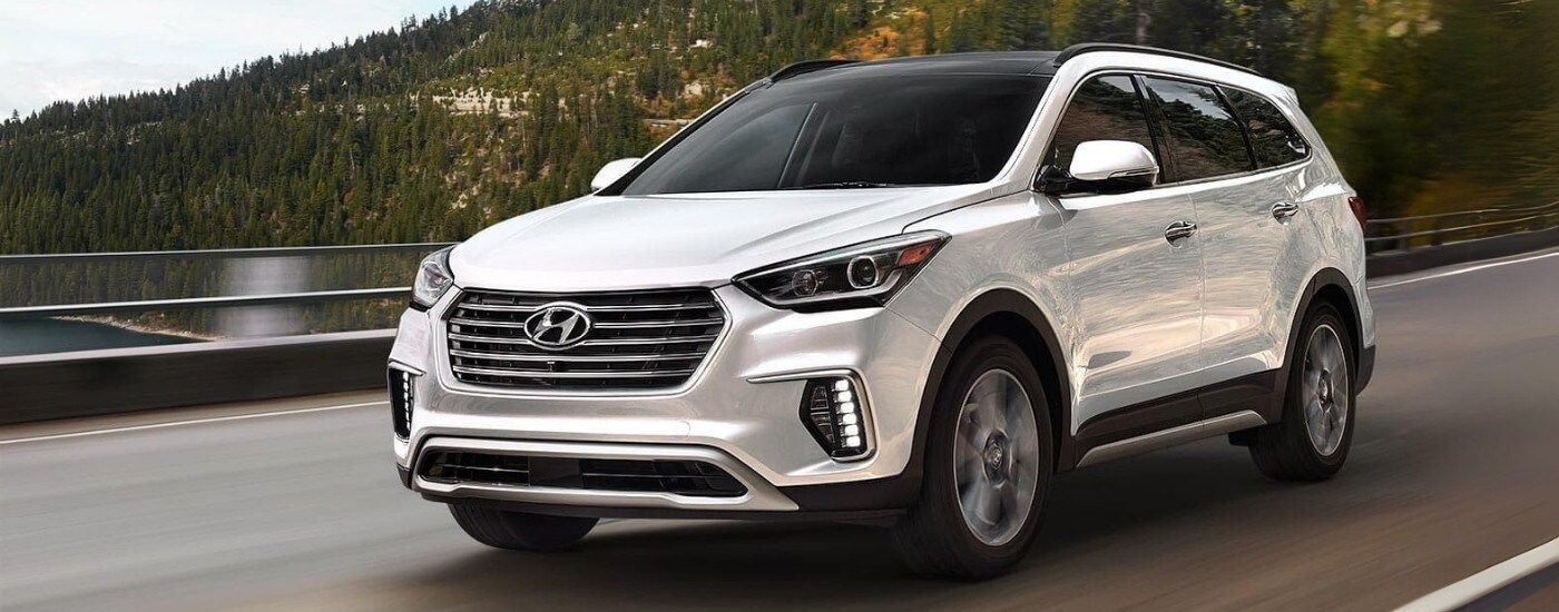 A white 2017 Hyundai Santa Fe driving past a lake.