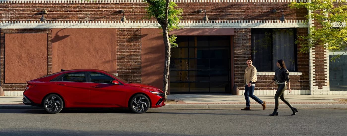 Two people walking towards a parked red 2025 Hyundai Elantra
