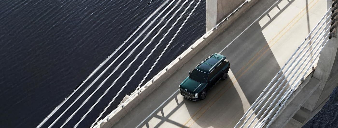 An aerial view of a green 2026 Hyundai Palisade for sale driving on a bridge near Weddington.