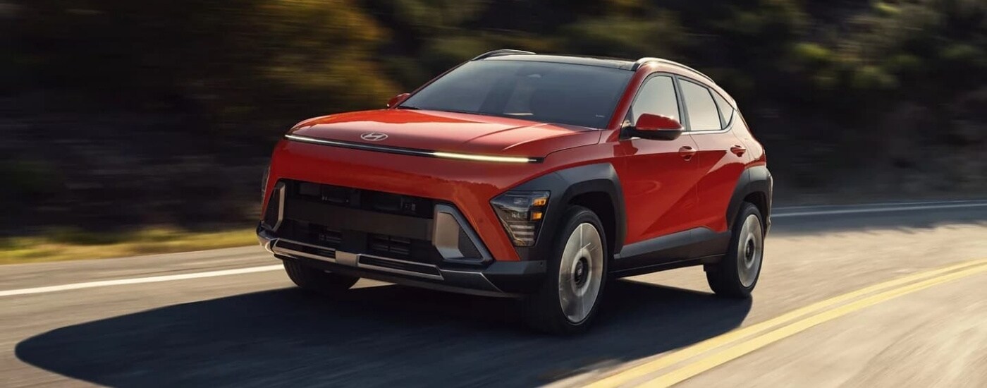 A red 2024 Hyundai Kona driving to a Hyundai dealer in Monroe.
