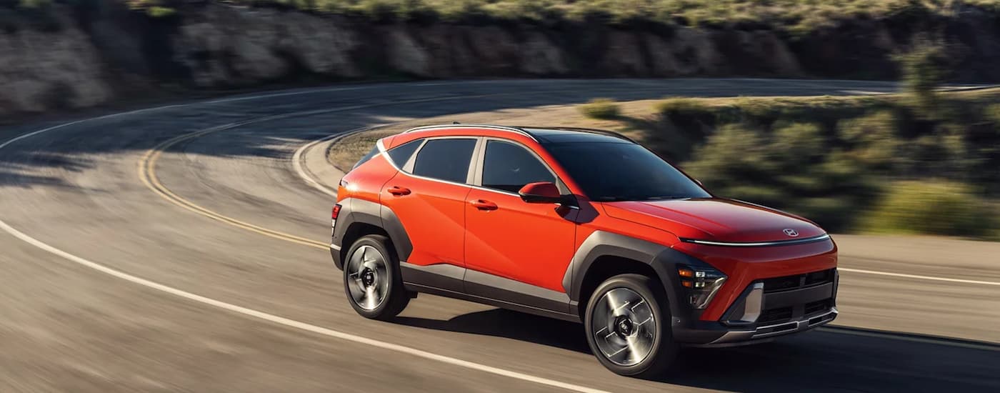 Red 2025 Hyundai Kona for sale near Matthews driving around a bend.