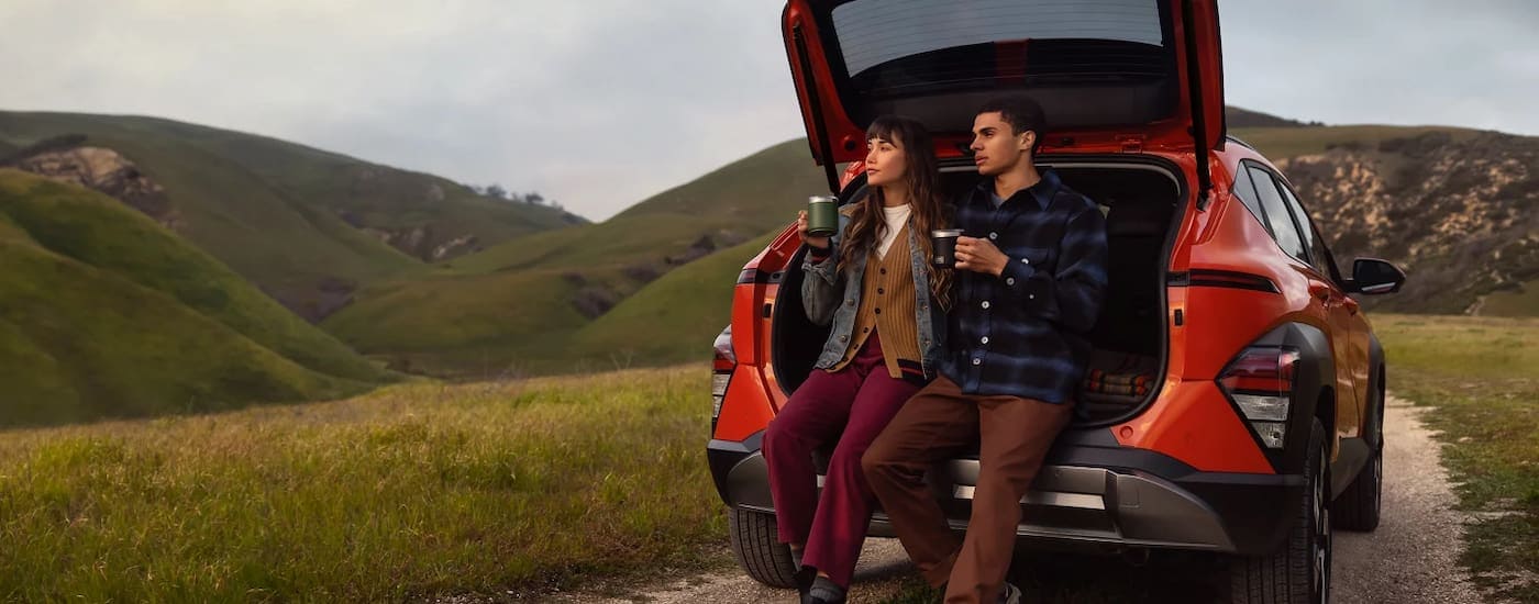 Two people sitting in the back of a red 2026 Hyundai Kona parked off-road.