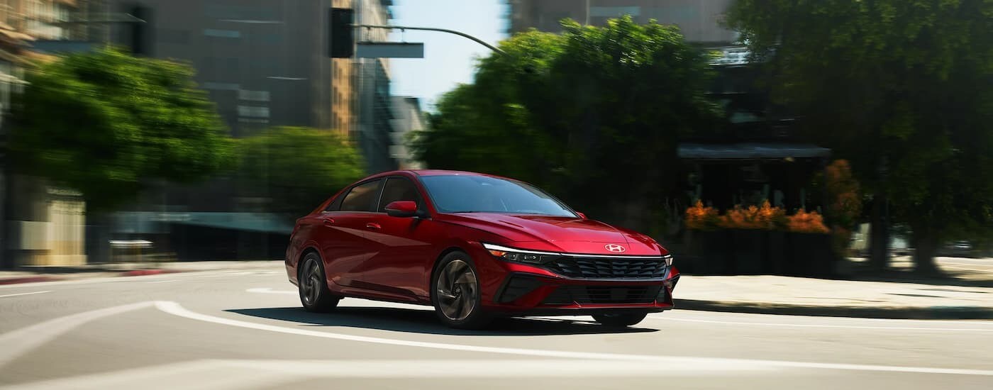A red 2025 Hyundai Elantra for sale driving on a city street.
