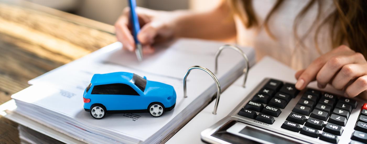 A person filling out paperwork next to a blue toy car.