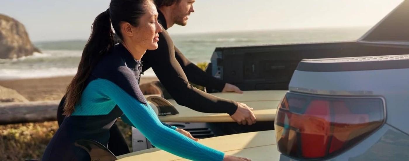 People putting surfboards in the bed of a blue 2022 Hyundai Santa Cruz.