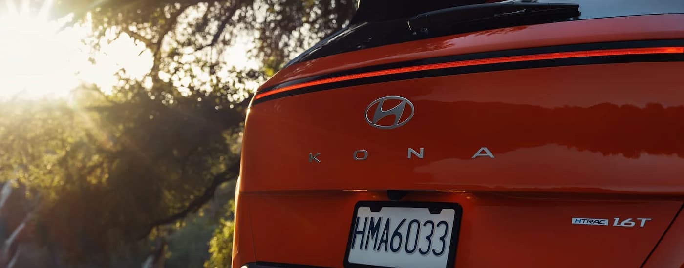 Rear of an orange 2025 Hyundai Kona parked near trees