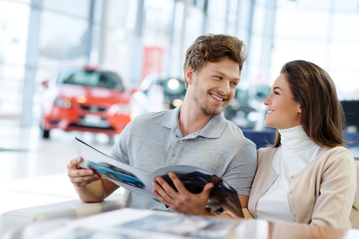 Excited Couple Reading Brochure of a new vehicle at a car dealership