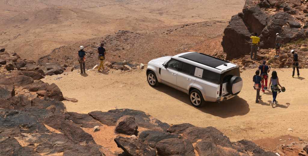 Group of people with a 2022 Land Rover Defender 130 on a cliff