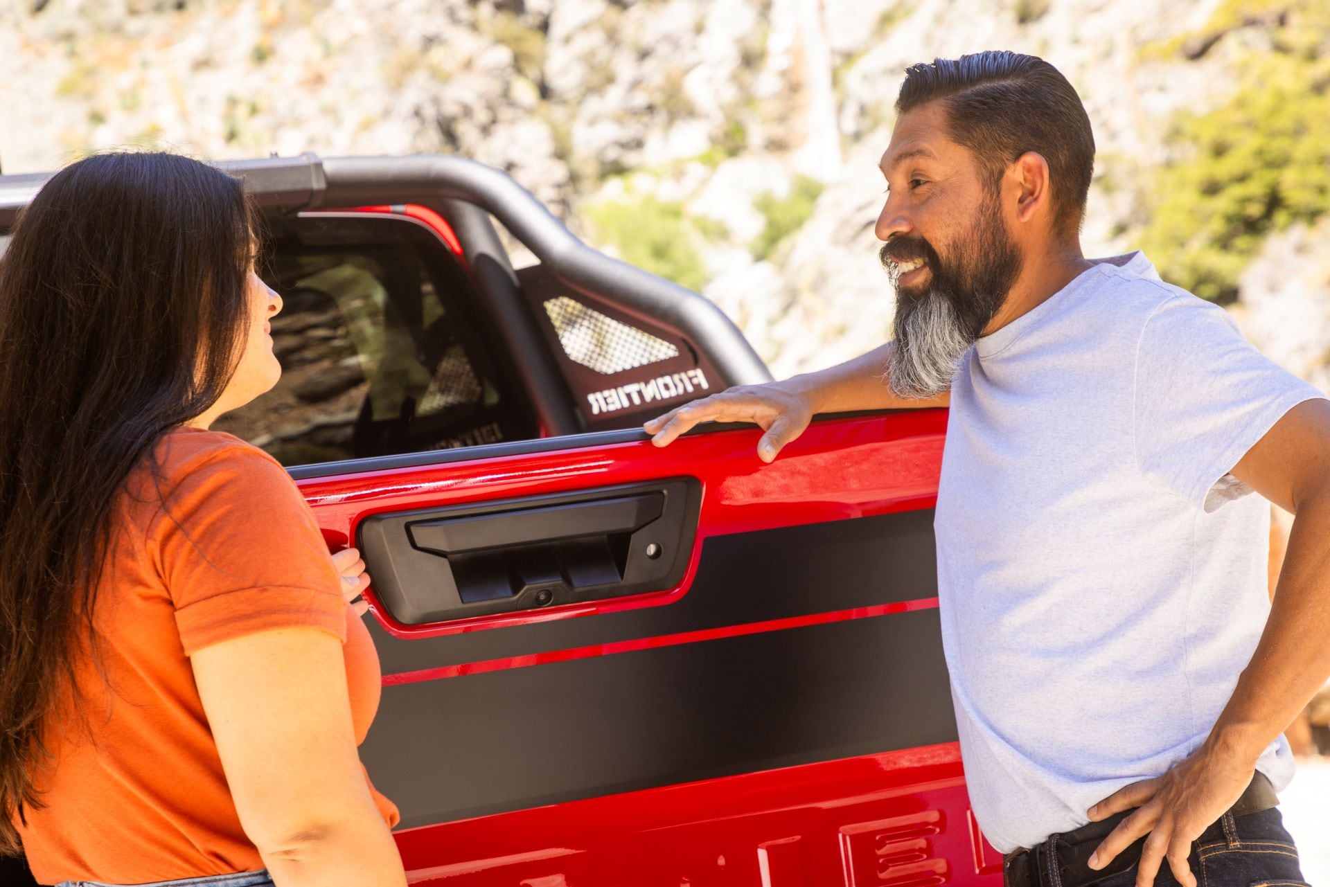 An Imperial Valley farmer standing behind a red used Nissan Frontier for personal use and work in agriculture, talking to a sales advisor at Imperial Valley Hyundai