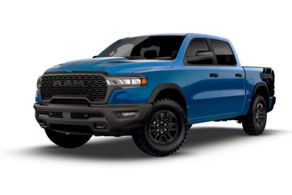 Front three-quarter view of a bright blue 2026 RAM 1500 Rebel off-road truck featuring an aggressive blacked-out grille, bed graphics, and rugged all-terrain tires.