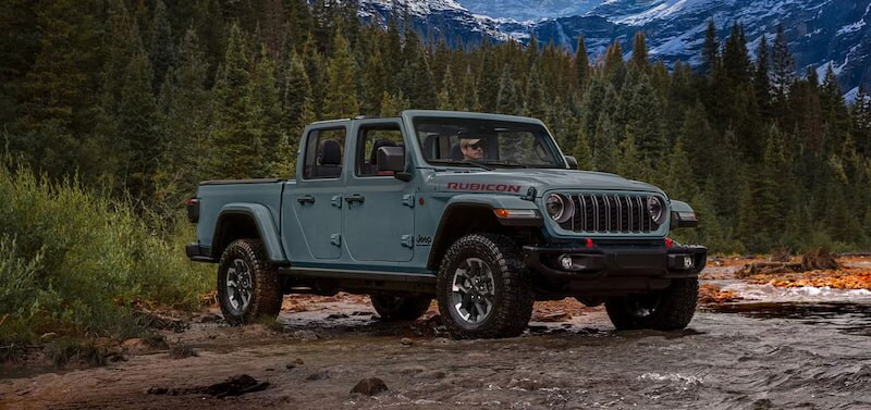 2026 Jeep Gladiator Rubicon parked beside a mountain river showcasing its off-road truck capability