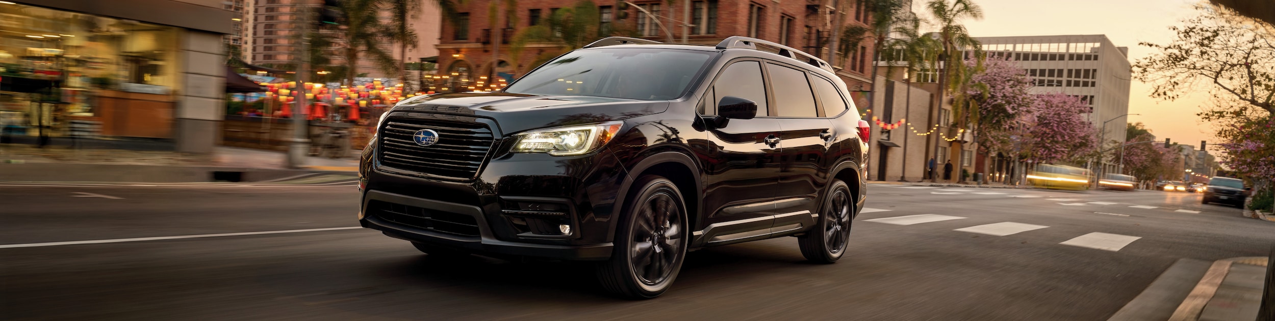 A black 2022 Subaru Ascent driving down a town street against an orange sunset.