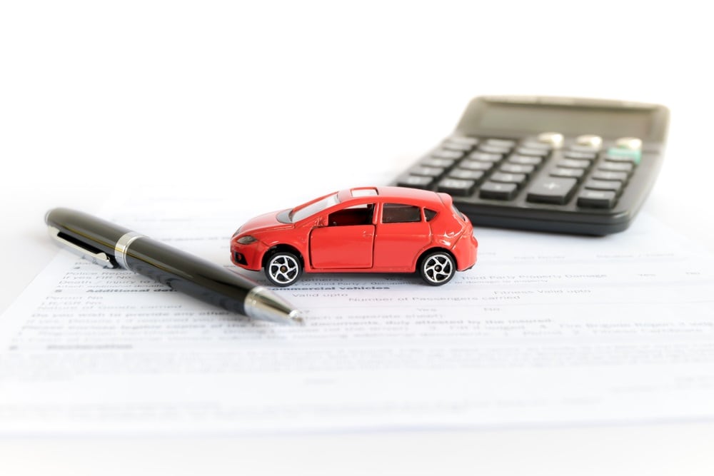 A pen, small red toy car, and a calculator laying on top of Subaru Ascent lease paperwork.