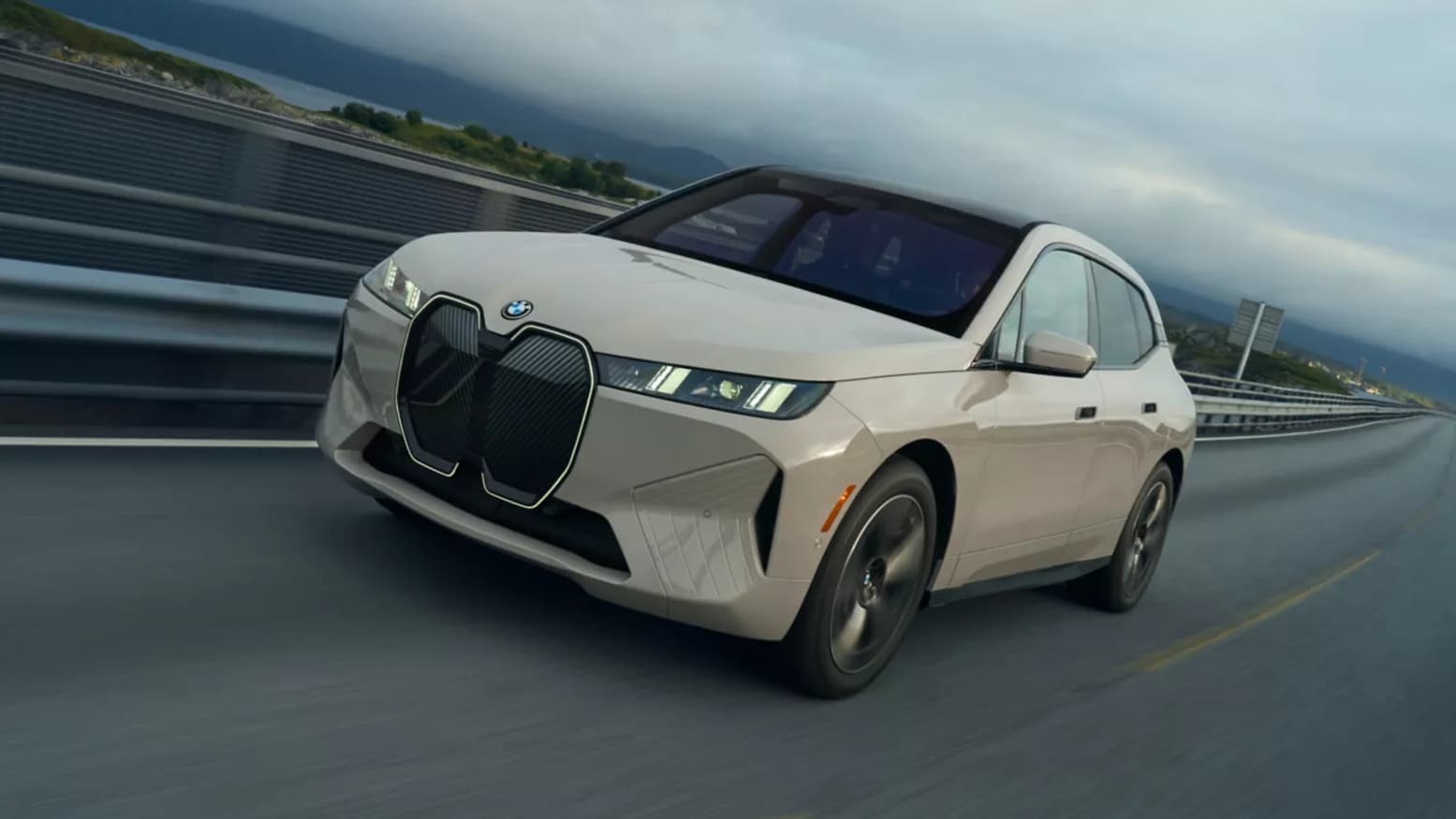 A front view of a light-colored BMW iX driving down the highway.
