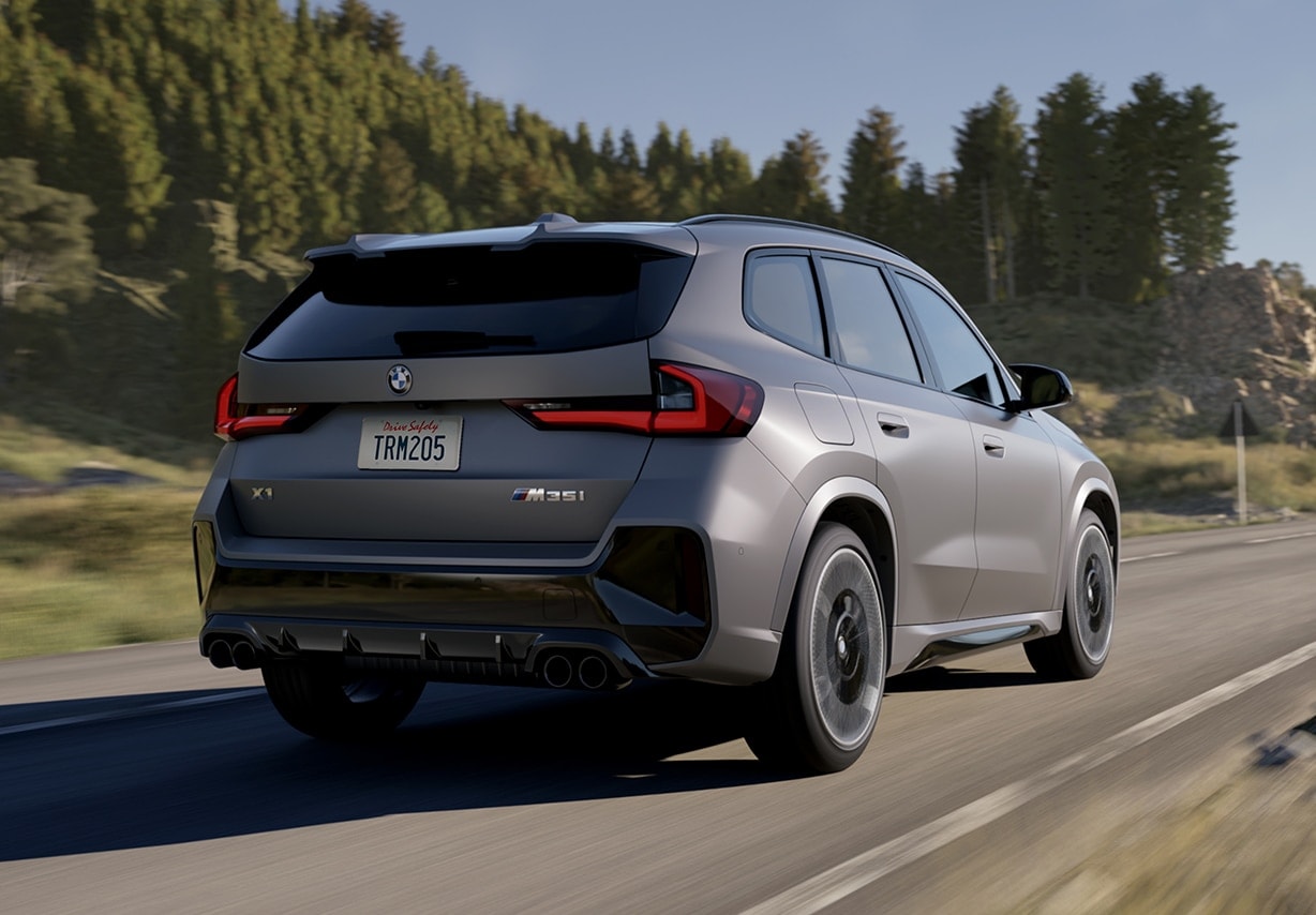 A gray 2025 BMW X1 driving quickly down the road near a forest. A gray 2025 BMW X1 driving quickly down the road near a forest.